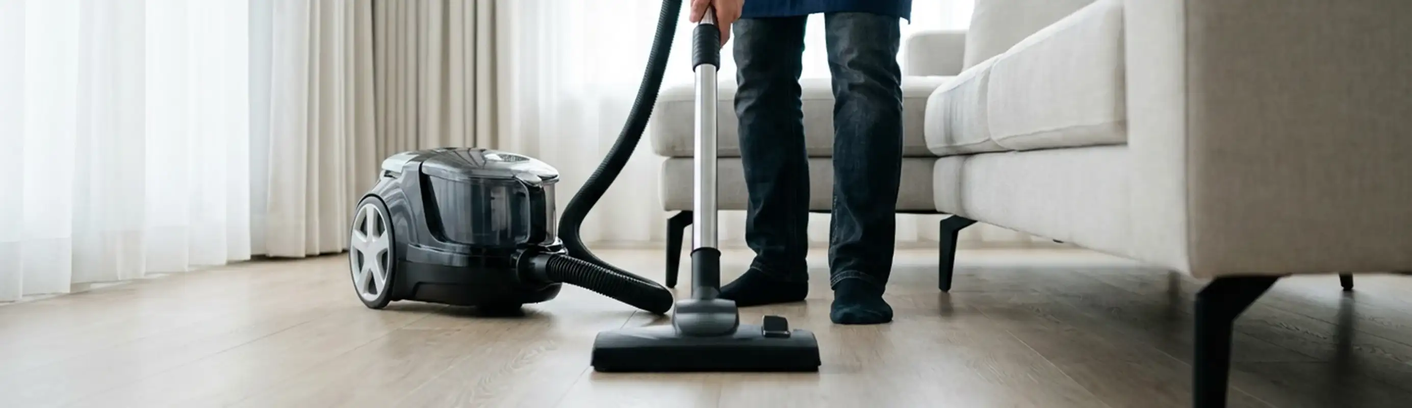 Professional house cleaner vacuuming a living room floor with a canister vacuum cleaner, Henderson, NV.