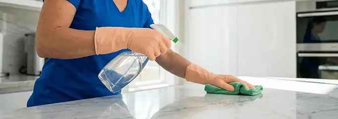Maid service worker spraying and wiping a kitchen countertop with a microfiber cloth for sanitizing, Henderson, NV.