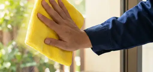 House cleaner wiping a glass window with a yellow microfiber cloth for streak-free cleaning, Henderson, NV.